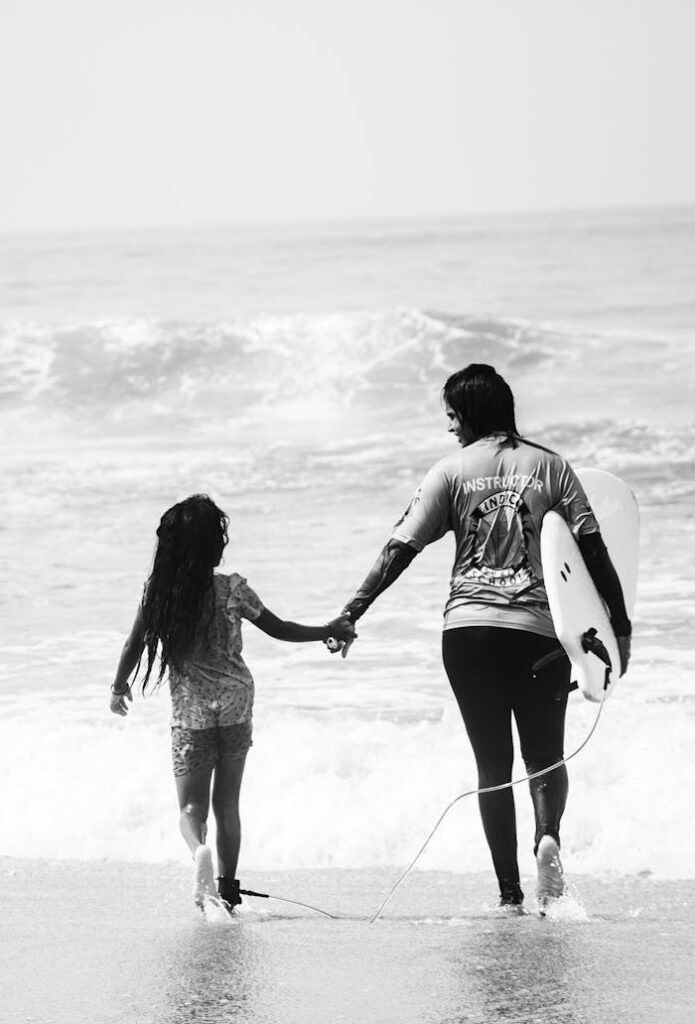 Black and white photo of a woman and child holding hands on a beach.