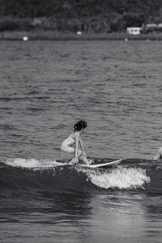 A child rides a small wave on a surfboard in this black and white photo.