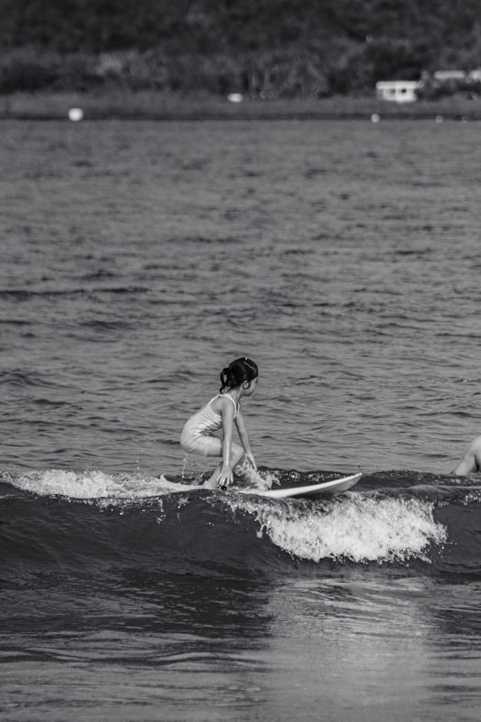 A child rides a small wave on a surfboard in this black and white photo.