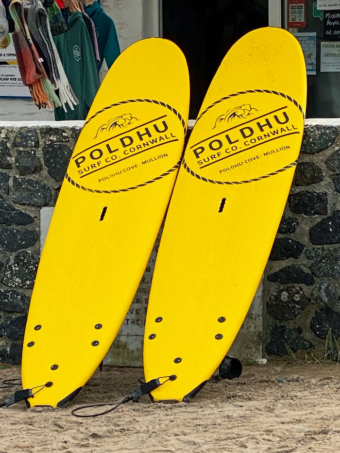 Two vibrant yellow surfboards leaning against a stone wall at Poldhu Cove, Cornwall, ready for adventure.
