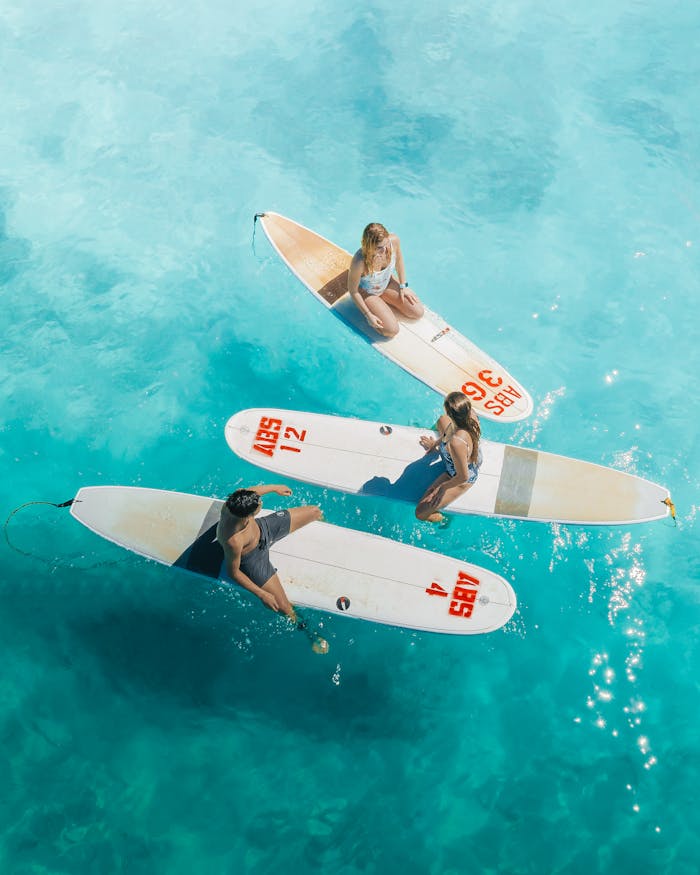Three surfers resting on their boards in crystal clear Hawaiian waters, showcasing vibrant ocean life.