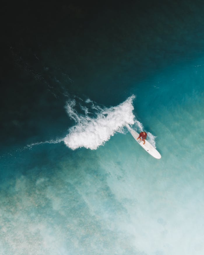 Dynamic aerial shot of a surfer navigating a wave in blue ocean waters, showcasing skill and adventure.