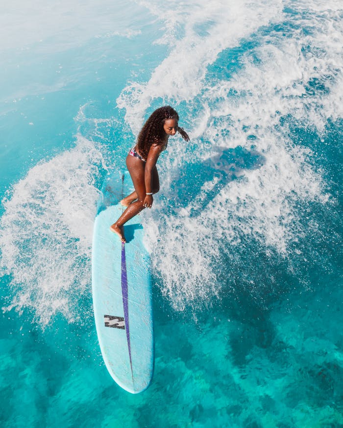 A woman skillfully surfs on a wave in the turquoise ocean, showcasing vibrant water sport action.